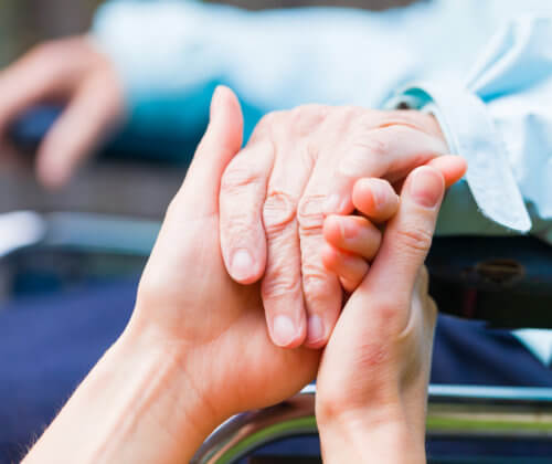 Close shot of senior in a wheel chair's hand being help by caregiver