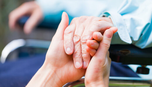 Close shot of senior in a wheel chair's hand being help by caregiver