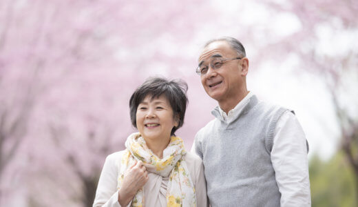 Smiling senior couple look off to the side as they stand in front of cherry blossom trees