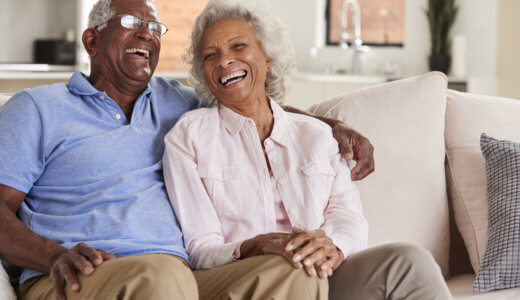 Senior Couple Sitting On Sofa At Home And Laughing Together