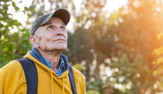 Senior man with backpack and baseball cap looking up while on a forest trail hike