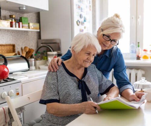 Woman and senior mother look over paperwork together at a kitchen table
