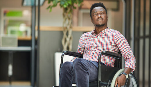 Male office worker in wheelchair looking off to the side with office building in the background
