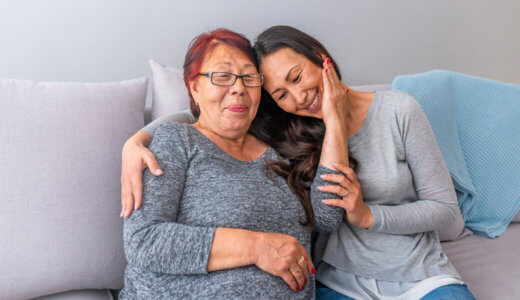 Mother and adult daughter sitting on a couch, mother caressing daughter's face