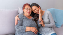 Mother and adult daughter sitting on a couch, mother caressing daughter's face