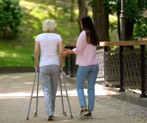 Woman with walker and young woman walking in a park