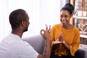 Smiling Young Couple Sitting On Sofa Communicating With Sign Languages